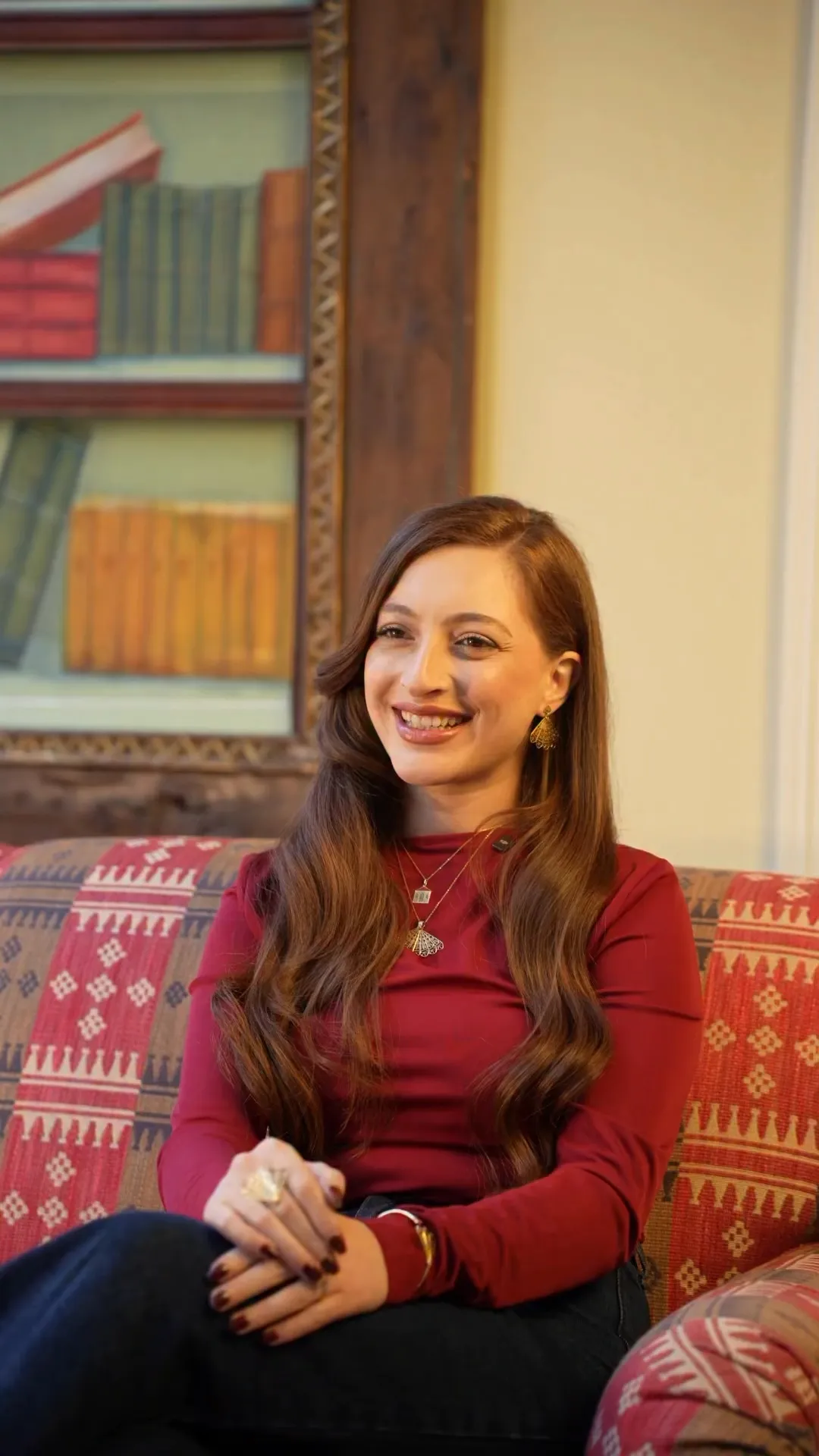 Woman in a red top and gold jewellery smiling on a patterned sofa — still from the Lamaro Fine Jewelry reel