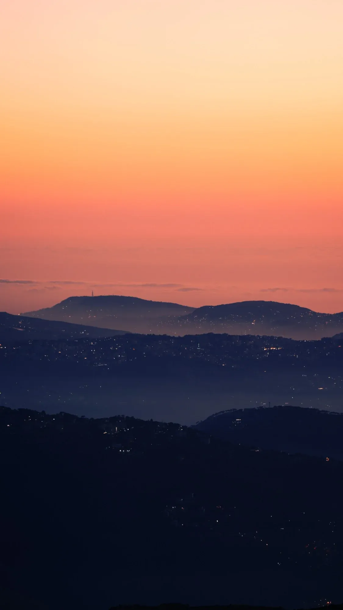 Sunset over layered mountain ridges seen from Zaarour, with town lights below