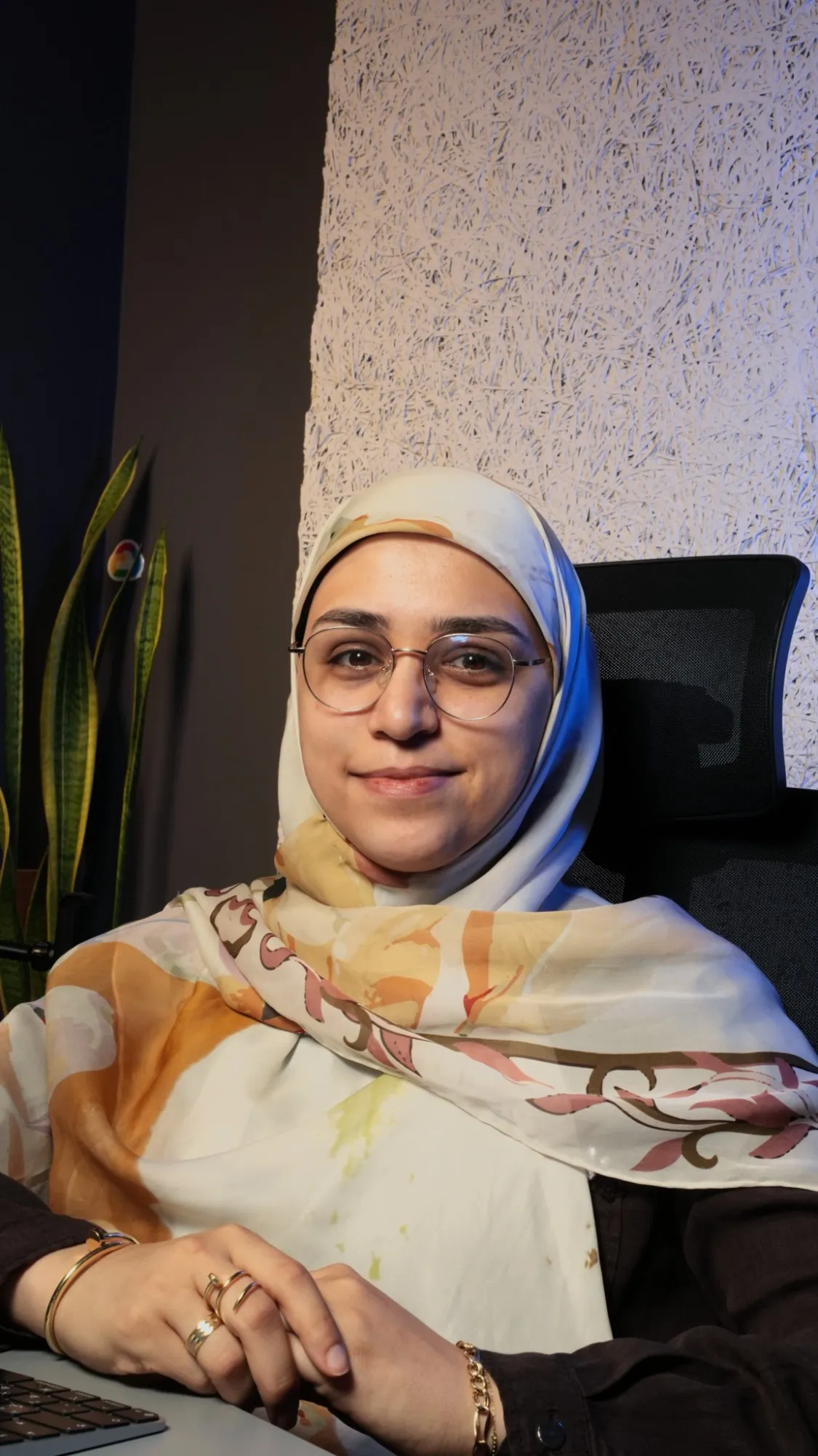 Woman in a floral headscarf and glasses smiling at her desk — still from the Lara Wehbi video